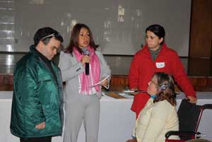 Foto com quatro pessoas. De p Alex Garcia, Dra. Scheila Lima, apoiadora Aline e Ftima Braum, da Associao dos Amigos Deficientes, sentada em cadeira de Rodas. Dra Scheila fala ao microfone e tem um documento nas mos.