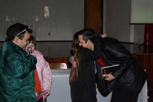 Nesta foto, Alex Garcia segura o microfone, sorri. Na frente dele o palestrante Marcos Henkes abraa uma jovem de cabelos castanhos, lisos e longos. Ele segura um livro na mo esquerda. Ao lado esquerdo de Alex, uma jovem da ONG DOWN observa. Todos esto usando roupas prprias de frio.